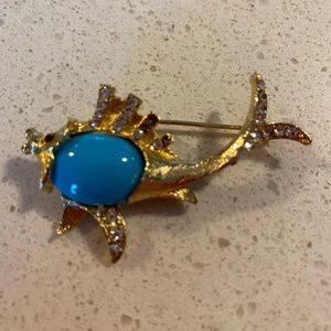 Gold tone fish pin with turquoise colored center stone, red garnet colored eyes